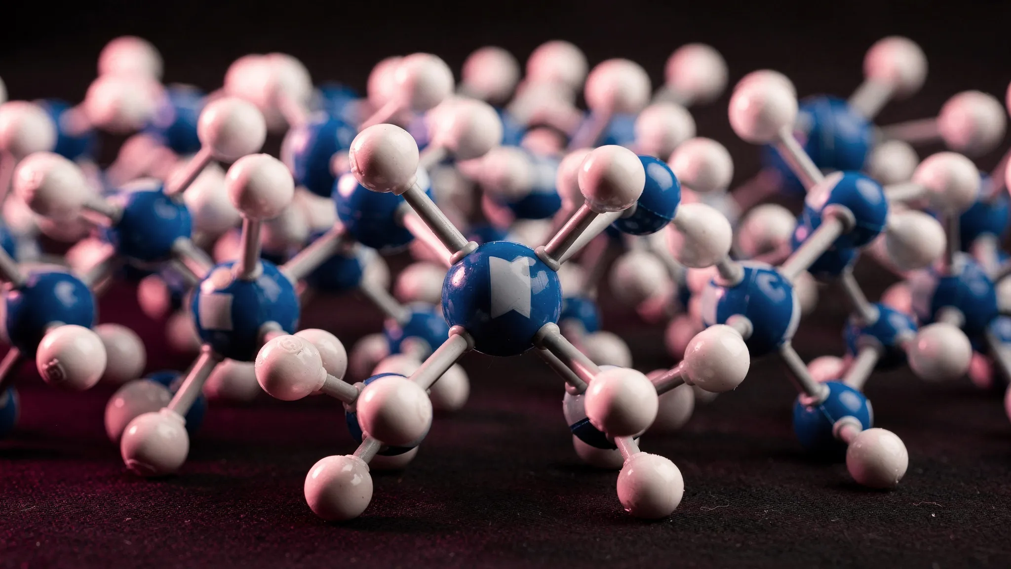 A ball-and-stick model of many small molecules packed together, blue central atoms bonded to white atoms, lit in deep magenta.
