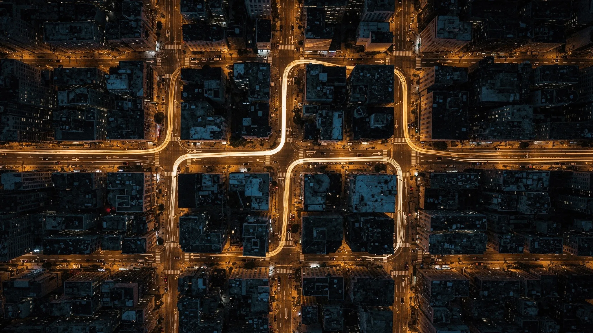 A night aerial view of a dense grid of city streets, a single glowing route winding through several crossings, lit in deep amber.